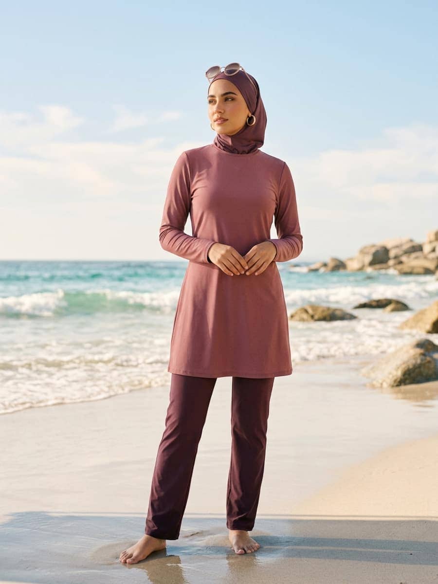 Femme portant un burkini prune couvrant avec un hijab de bain assorti au bord de la mer