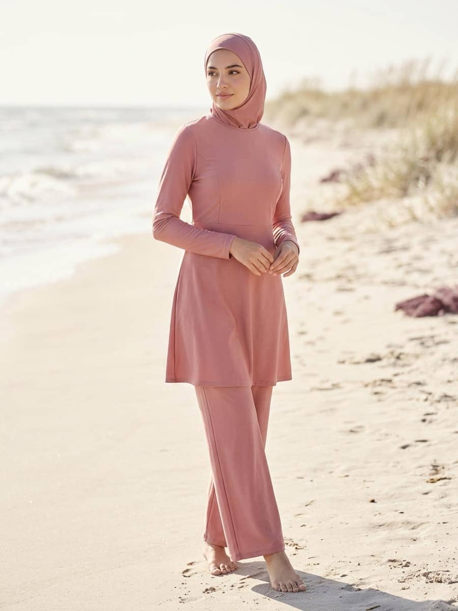 Femme en ensemble de bain pudique deux pièces rose, tunique longue et pantalon de bain large, avec hijab